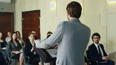 vista posteriore dell'altoparlante caucasico dell'uomo d'affari su un podio che parla in una sala conferenze davanti a molte persone