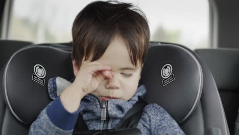 un niño de raza mixta somnoliento viaja en un asiento de coche para bebés