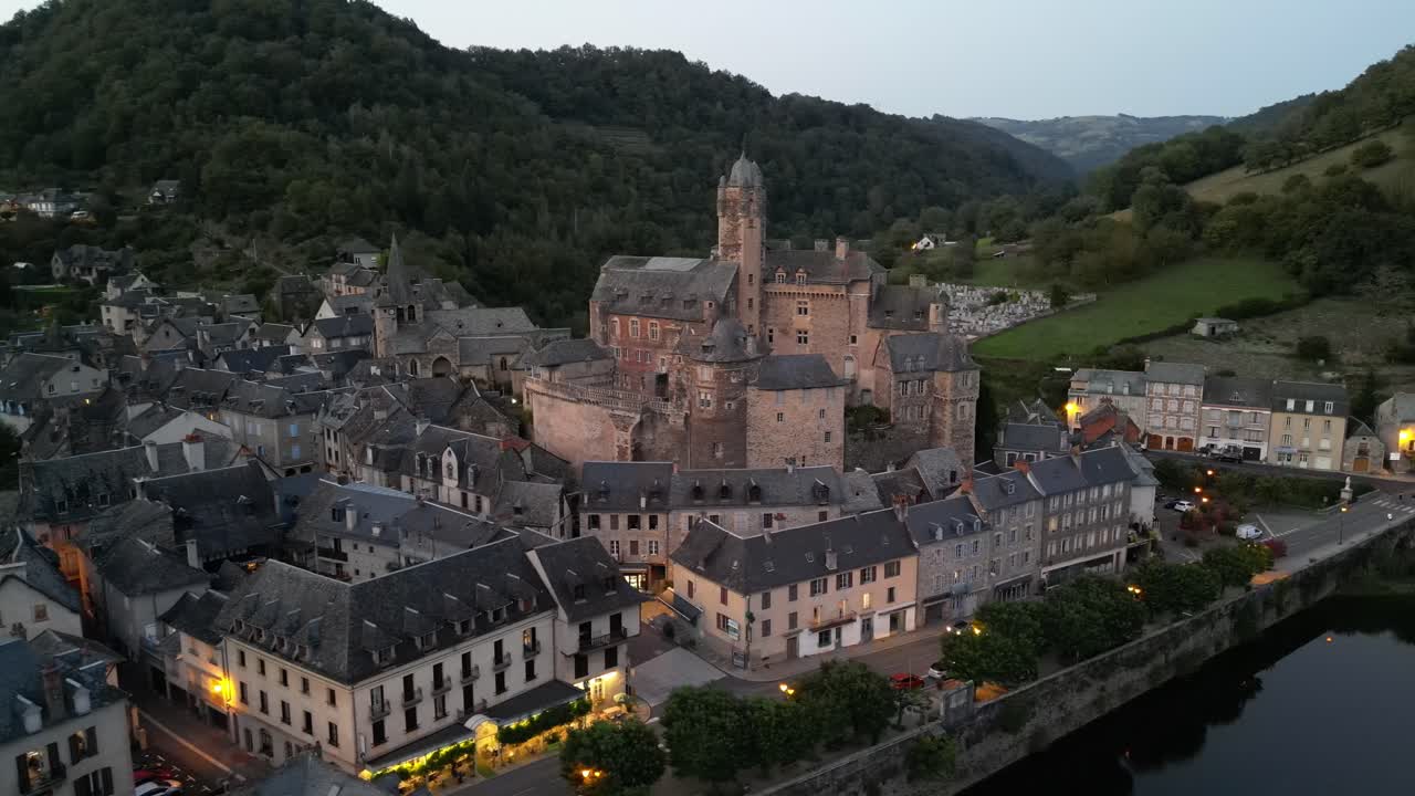Drone aerial view in France countryside small old medieval town and a castle over stone bridge on a river in a green mountain valley forest at sunset in Estaing