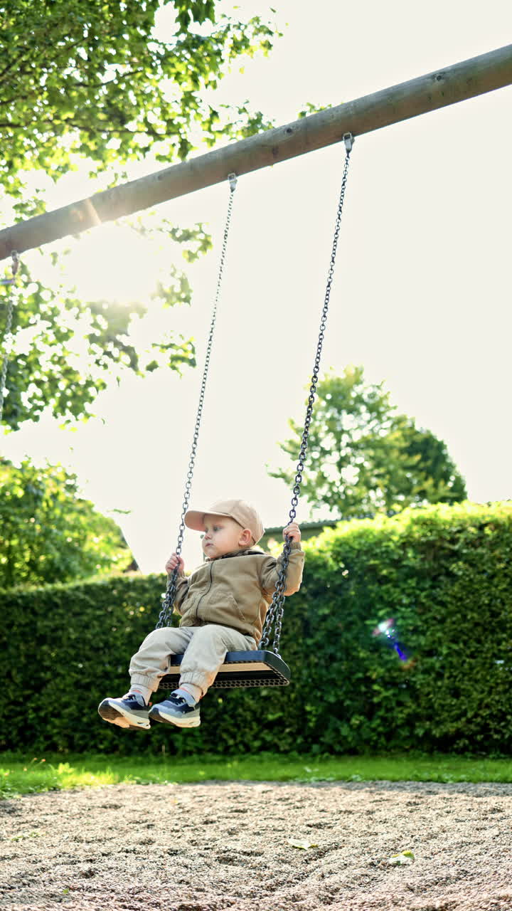 Bambino felice sull'altalena al parco in una splendida giornata estiva. Un bambino sorridente si dondola in un parco giochi in una calda giornata d'estate. Bambino all'aperto in un parco giochi.