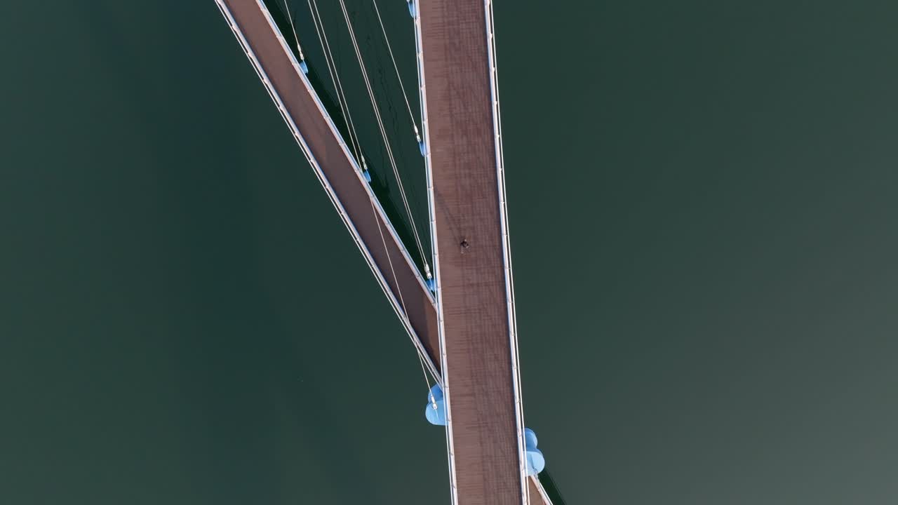Aerial tracking shot of a person walking on a curved urban bridge with strong shadows in Masan Marine Park, South Korea.