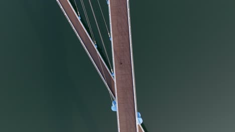 aerial tracking shot of a person walking on a curved urban bridge with strong shadows in masan marine park, south korea.