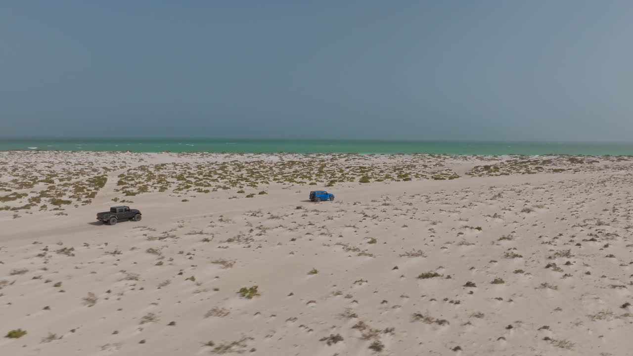 Two pickup trucks on a remote beach in Bar Al Hikman, Oman, near turquoise waters
