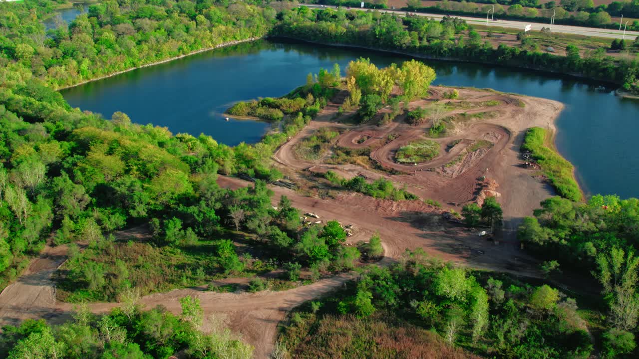 Pleasant Motocross Off Road Track next to a Lake with a Motorcyclist Racing in a Sunny Day, Approaching Shot