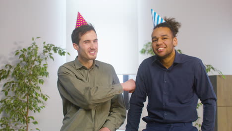 Portrait-Of-And-American-Men-With-Party-Hat-Greeting-And-Then-Smiling-At-The-Camera-At-The-Office