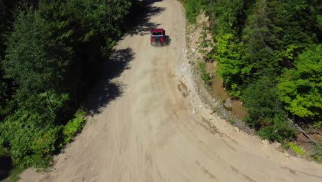 red off-road vehicle drifting on dirt terrain in beautiful green forest captured by drone