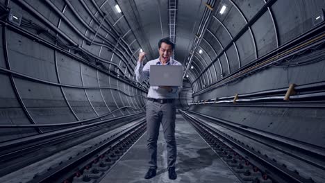 full body of an asian male professional worker standing with his laptop in underground subway tunnel, he raises his fist up with screaming goal