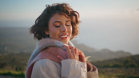 smiling woman windblown hair posing at cold evening coastal hill closeup.