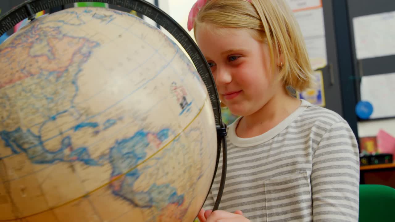 Front view of Caucasian schoolgirl studying globe at desk in classroom at school 4k