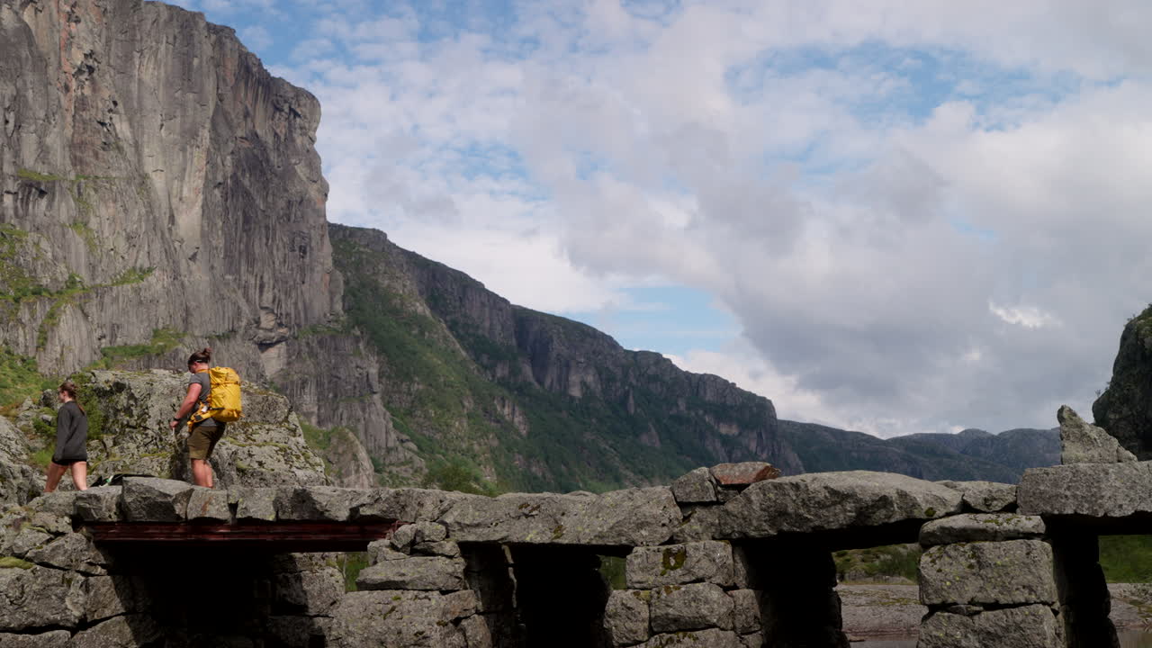 Hiking couple with dog cross stone bridge over river in rugged Norway landscape