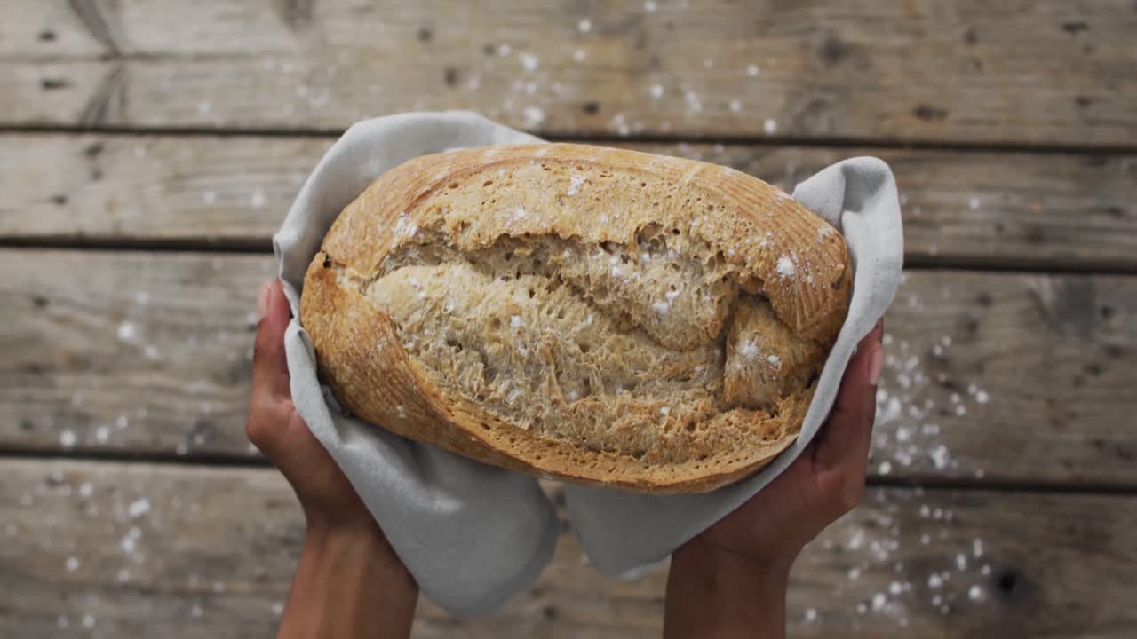 Video of bread in hands on wooden worktop seeing from above