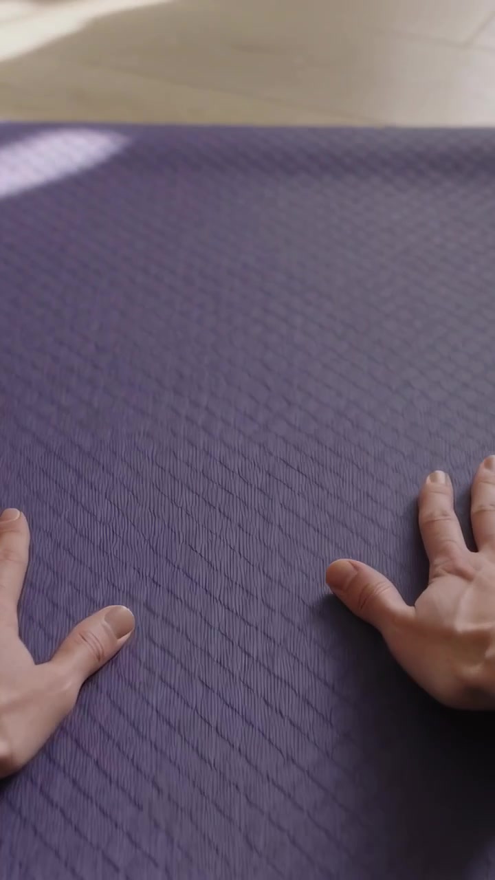 Video vertical: Colocando las manos y ajustando el agarre en una esterilla morada en casa para yoga, con un parche de luz apareciendo.