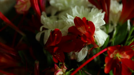 ingrandito in dettaglio un grande mazzo di fiori rossi e bianchi ed elementi decorativi verdi in un vaso di vetro decorato con carta intorno su uno sfondo scuro