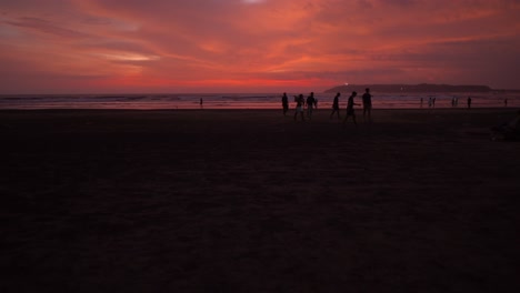 group of young people walking on sand and leaving the beach at dusk with red sky