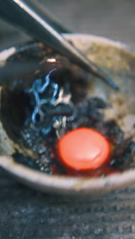 cu: skilled jeweler takes hot gold metal drop from special fireproof cup with tweezers on asbestos sheet in craft workshop closeup