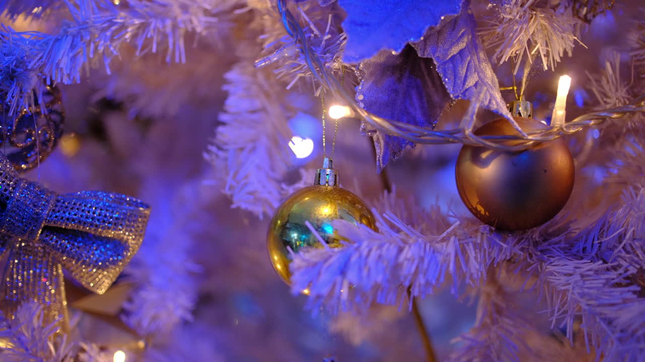 Golden christmas baubles and glowing fairy lights decorating a festive white artificial tree