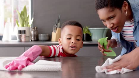 african american mother and son cleaning countertop in kitchen, slow motion