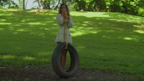 in a tropical park, a curly-haired girl enjoys the sunny weather swing on a tire