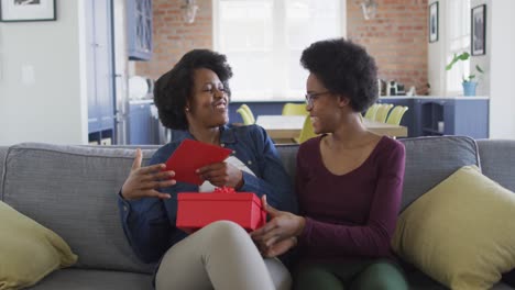 Feliz-Madre-E-Hija-Afroamericana-Sentadas-En-El-Sofá,-Dando-Regalos