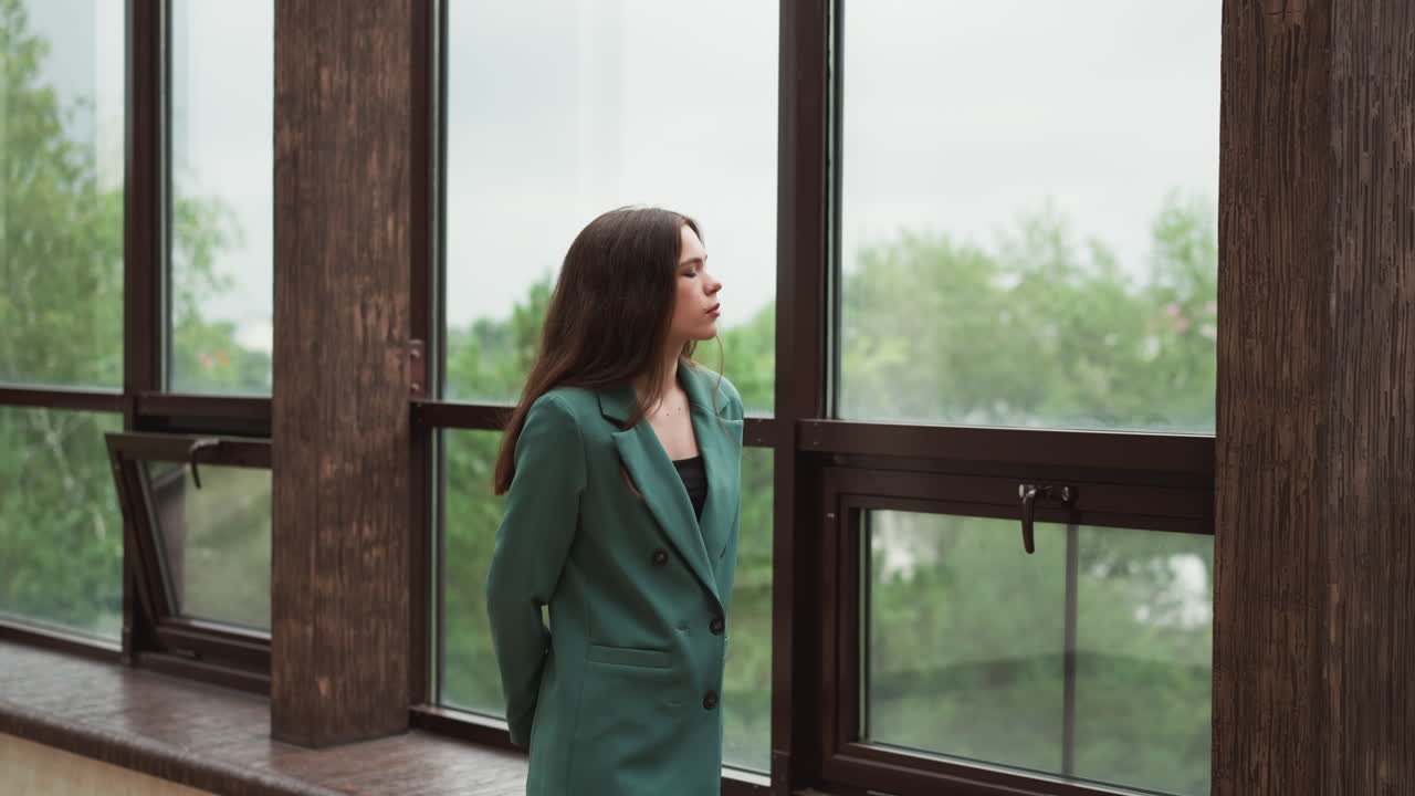 Woman leader strolls along expansive windows. Lady brows furrowed in contemplation over dwindling client contracts. Financial uncertainty about future