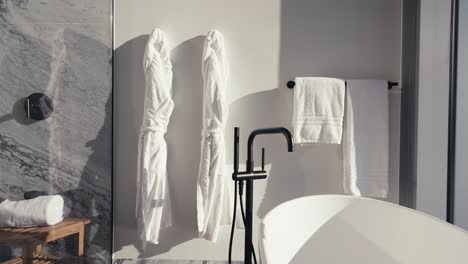 panning shot of white towels and robes hanging on the wall next to a white free standing tub in a high rise condo bathroom