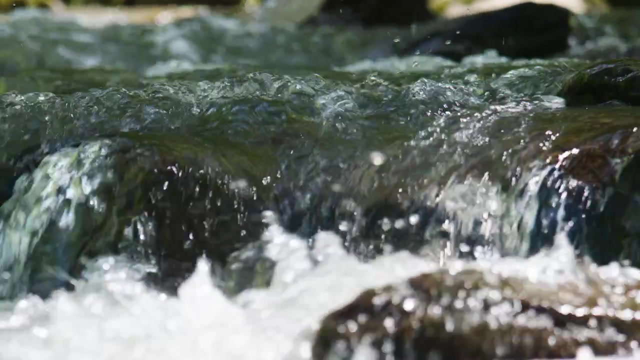 Un chiaro ruscello di montagna scorre su rocce lisce. L'acqua schizza e increspa con energia naturale. La luce del sole si riflette sulle superfici bagnate, evidenziando il movimento. Ideale per natura, viaggi