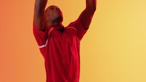 african american male rugby player catching rugby ball over orange lighting