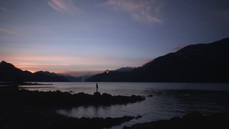 Persona-Lanza-Una-Sola-Linterna-De-Papel-Al-Cielo-Nocturno-Sobre-Un-Lago-De-Montaña