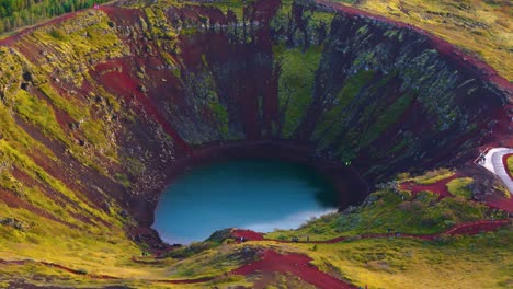 kerid crater in iceland, water at the bottom, red earth, vegetation and a fir forest in the background