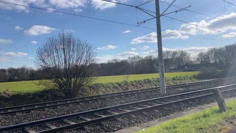 Beautiful-free-2-track-railway-line-with-high-voltage-pylons-in-good-weather-with-a-large-field-and-trees-in-the-background