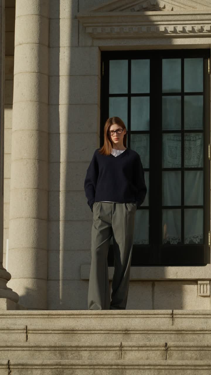 Vertical full body shot of a fashionable Ukrainian woman in glasses posing on the wide stone steps of an elegant building exterior