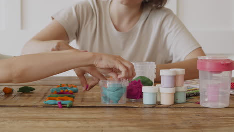 close up detail of the hands of a woman and her daughter modeling letters with colored plasticine