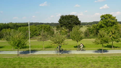 Couple-cycling-on-countryside-road-with-tree-alley-in-Moravia,-summer