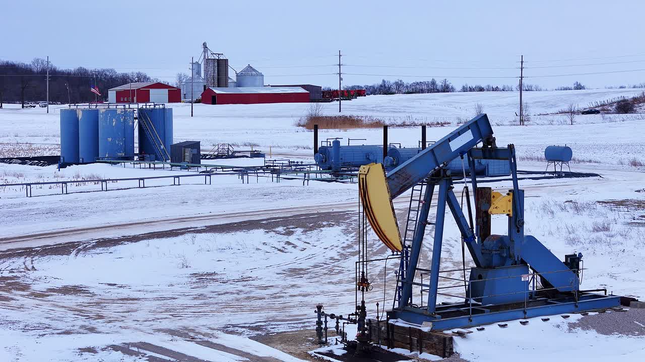 Pompa di estrazione petrolifera in funzione vicino a edifici agricoli in un campo innevato del Michigan, USA