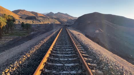 muévase en el ferrocarril al atardecer en irán medio oriente asia persia yazd ardakan cerca del remoto pueblo oasis abandonado con montañas mina de oro mina de hierro y jardín de palmeras en el desierto de lut
