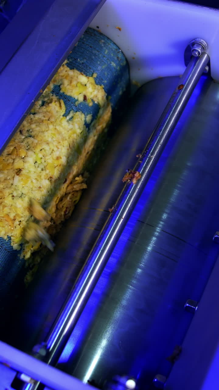Squeezed apple pieces are sent between rotating shafts. Apple juice production at the modern food factory. Vertical video