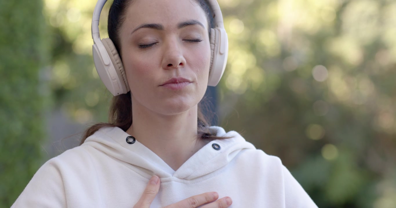 Donna che guarda un telefono viola, abbassandolo, con le mani sul petto in giardino, respirando per calmarsi, con le cuffie