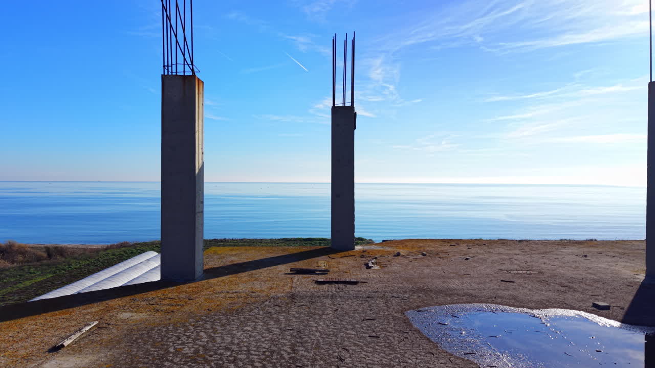 Serre bianche su un campo verde con colonne di cemento incompiute vicino alla costa. Costruzione di un edificio a più piani. Vista aerea