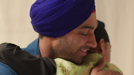 close up studio shot of sikh father embracing son both wearing turbans against plain background 4