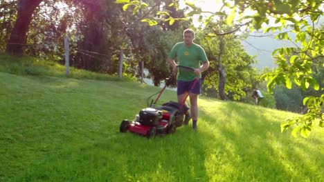 Hombre-Recortando-Su-Césped-Verde-Alrededor-De-Su-Casa-Con-Una-Segadora-Rotativa-De-Gasolina-Roja