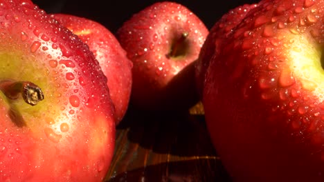 primer plano de frutas de manzana rojas con gotas de agua en una mesa de madera sobre un fondo negro