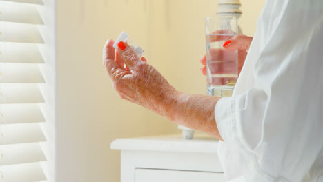 Vista-Lateral-De-Una-Mujer-Caucásica-Mayor-Tomando-Medicina-Con-Un-Vaso-De-Agua-En-La-Cama-En-El-Dormitorio-4k