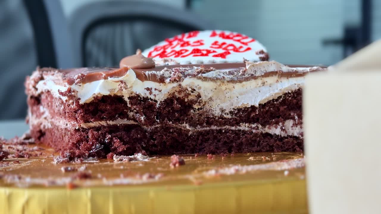 Primo piano di una deliziosa torta al cioccolato a fette con strati di crema e glassa. Il dessert è posizionato su una base dorata in un ambiente interno luminoso, che mette in risalto texture ricche e dettagli dolci.