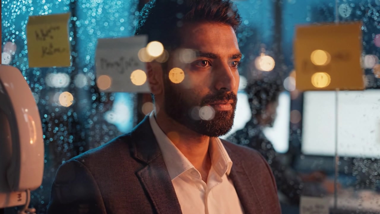 Professionista pensieroso che riflette su idee sullo sfondo di un paesaggio urbano piovoso con Post-it in un ambiente d'ufficio di notte.