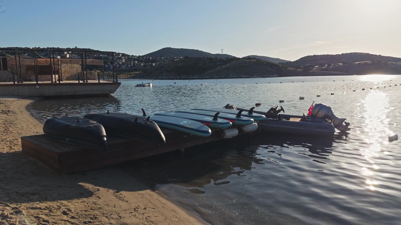 Motoscafi gonfiabili e kayak ormeggiati su una sponda soleggiata del lago con montagne sullo sfondo e acqua blu limpida.