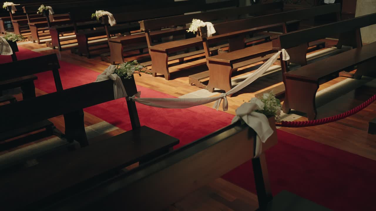 교회 안 붉은 카펫이 깔린 통로를 따라 흰색 천과 꽃으로 장식된 나무 의자가 놓여 있어요.