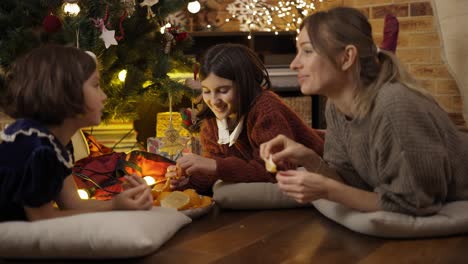 Mom-and-two-daughters-having-good-times-together,-taking-mandarins-under-Christmas-and-talk