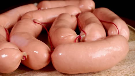 many raw frankfurter sausages on cutting board on a dark background rotate slowly.