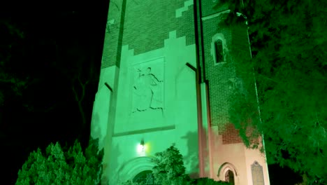 Beaumont-Tower-on-the-campus-of-Michigan-State-University-lit-up-at-night-in-green-in-honor-of-the-victims-of-the-February,-2023-mass-shooting-with-video-tilting-close-up-tilting-up