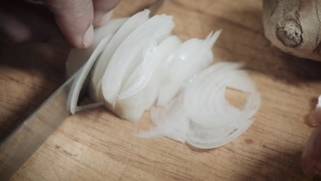 Die-Hand-Des-Küchenchefs-Schneidet-Schnell-Weiße-Zwiebeln-Auf-Einem-Holzschneidebrett-Mit-Einem-Messer